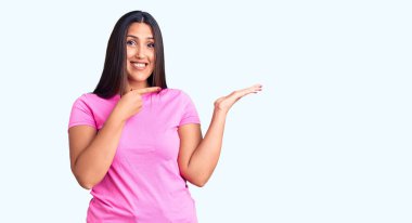 Genç, güzel, esmer, sıradan bir tişört giyen kadın kameraya hayret ediyor ve gülümsüyor.. 