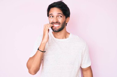 Yakışıklı, beyaz tişört giyen, gergin ve gergin görünen elleri ağzında, tırnaklarını yiyen bir İspanyol. anksiyete. 