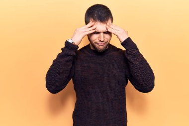 Genç, yakışıklı bir adam, elleri kafasında sıradan bir kazak giyiyor. Stres yüzünden baş ağrısı çekiyor. migren ağrısı. 