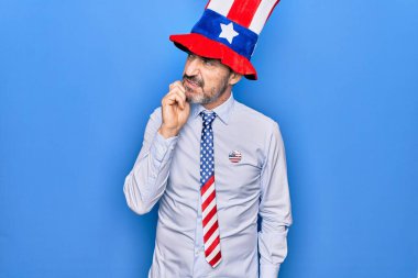 Orta yaşlı, yakışıklı, vatansever, şapkalı ve kravatlı bir adam mavi arka planda şüpheye odaklanmıştı.