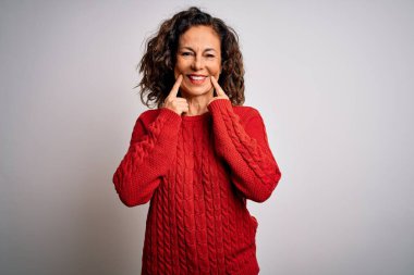 Orta yaşlı esmer kadın izole edilmiş beyaz arka planda dikiliyor ağzı açık gülümsüyor, parmakları işaret ediyor ve neşeli bir gülümseme sergiliyor.