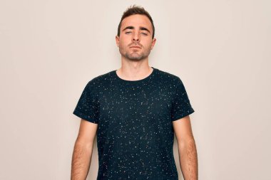 Mavi gözlü, beyaz arka planda duran ve yüzünde ciddi bir ifade olan sıradan tişörtler giyen genç yakışıklı bir adam. Basit ve doğal bir şekilde kameraya bakıyorsun..