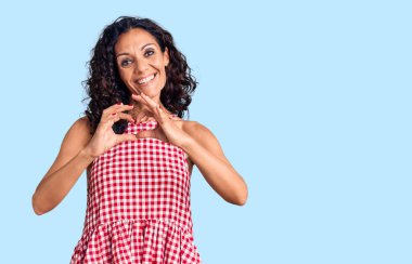 Orta yaşlı, kolsuz tişört giyen güzel bir kadın. Sevgiyle gülümsüyor. Elleriyle kalp sembolü ve şekli gösteriyor. romantik kavram. 