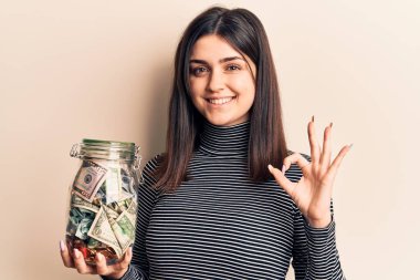 Bahşiş kavanozu tutan genç ve güzel bir kız parmaklarıyla imza atıyor, gülümseyerek mükemmel bir sembol oluşturuyor. 