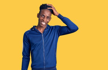 Genç Afro-Amerikan erkek spor giyer, gülümser, saçlarına dokunur, el hareketi yapar, çekici ve modaya uygun poz verir. 