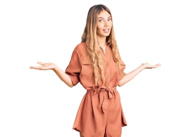 Sarı saçlı, yaz tulumu giyen, kafası karışık, elleri ve kolları havada beyaz bir kadın. şüphe kavramı. 