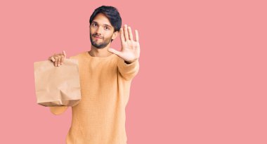 Yakışıklı ispanyol adam, elinde paket kağıdı, elinde açık elle dur işareti yapıyor. Ciddi ve kendinden emin bir ifadeyle, savunma jesti. 