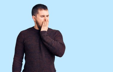 Gündelik kazak giyen genç yakışıklı adam ağzıyla esnemekten sıkıldı. Huzursuz ve uykulu.. 