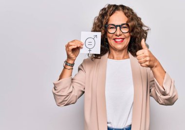 Orta yaşlı, güzel bir kadın elinde kağıt ile cinsiyet eşitliği konsepti mesajı taşıyor mutlu ve olumlu gülümsüyor, başparmağıyla mükemmel ve onay işareti yapıyor.