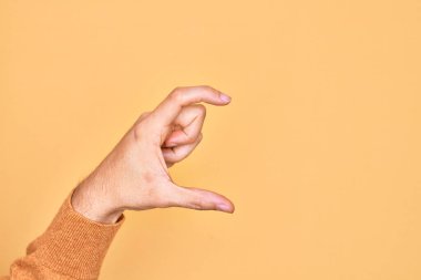 İzole edilmiş sarı arka plan üzerinde parmaklarını gösteren beyaz bir adamın eli. Görünmez bir şeyi alıp, parmaklarıyla uzayı gösteren bir nesneyi tutuyor.