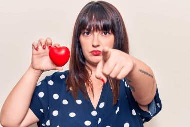 Kalbini tutan genç ve iri bir kadın kamerayı işaret ediyor ve sen kendine güvenen ciddi bir hareket yapıyorsun. 