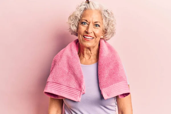 Senior grey-haired woman wearing sportswear and towel with a happy and cool smile on face. lucky person.
