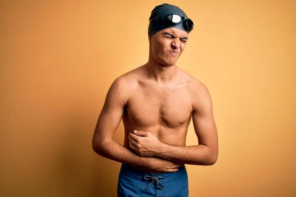 年轻英俊男子赤身裸体 身穿泳衣 头戴浅黄色的泳帽 双手放在肚子上 因为消化不良 痛苦不堪 阿切概念 — 图库照片