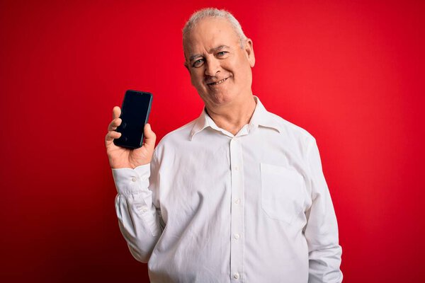 Middle age hoary man holding smartphone showing screen over isolated red background with a happy face standing and smiling with a confident smile showing teeth