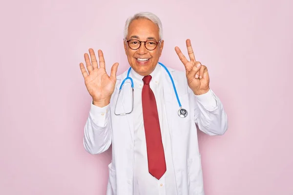 中年シニア白髪医者男身に着けています聴診器と専門医療コートショーと指番号7で指摘しながら笑顔自信と幸せ — ストック写真