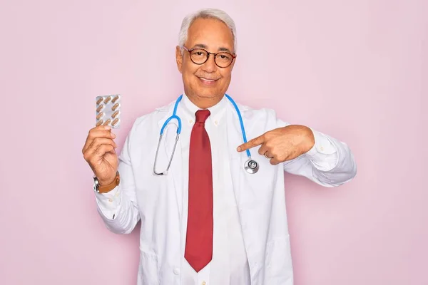 中年シニア白髪医者男保持処方薬上のピンクの背景とともに驚き顔ポインティング指へ彼自身 — ストック写真