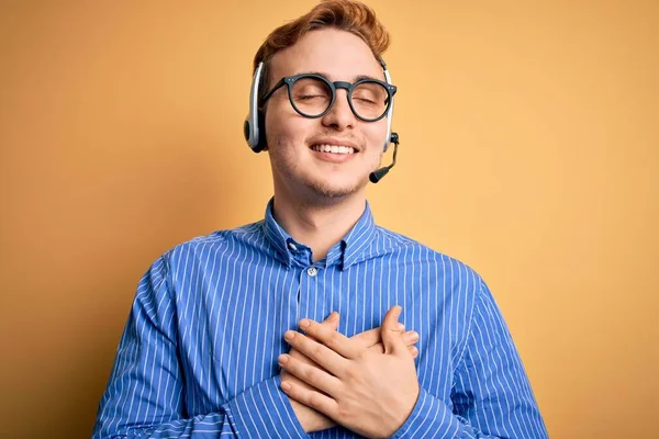 年轻英俊的红头发呼叫中心探员戴眼镜工作时 戴着耳机 双手放在胸前 闭上双眼 脸上挂着感激的手势 健康概念 — 图库照片