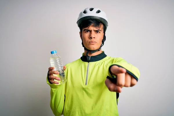 Young handsome cyclist man wearing security bike helmet drinking bottle of water pointing with finger to the camera and to you, hand sign, positive and confident gesture from the front