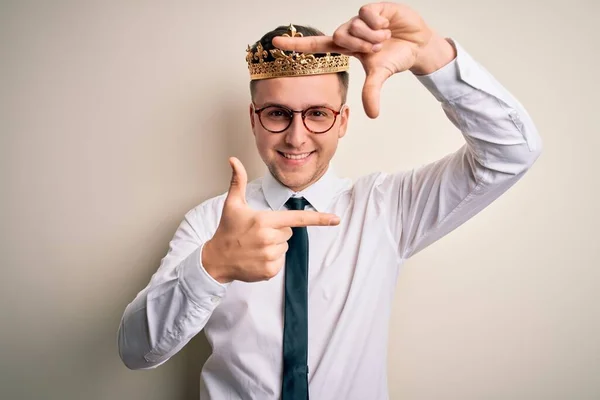 孤立した背景に黄金の冠を身に着けている若いハンサムな白人ビジネスマンは幸せな顔を持つ手と指でフレームを作り笑顔 創造性と写真の概念 — ストック写真