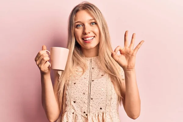 Young Beautiful Blonde Woman Holding Coffee Doing Sign Fingers Smiling — Stock Photo, Image