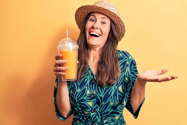 若いです美しいブルネット女性を身に着けています夏の帽子を飲みますオレンジジュースのガラス幸せな笑顔と受賞式とともに上げ手 — ストック写真