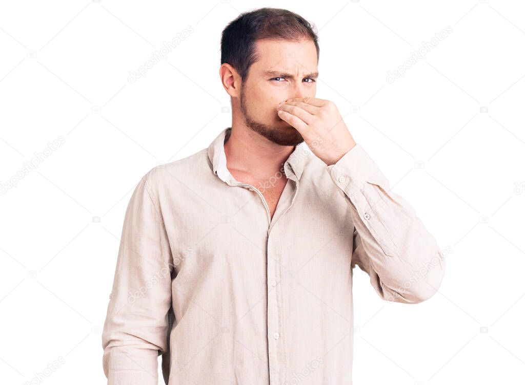 Young handsome caucasian man wearing casual clothes smelling something stinky and disgusting, intolerable smell, holding breath with fingers on nose. bad smell 