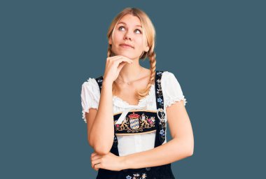 Oktoberfest elbisesi giymiş, eli çenesinde soru soran güzel sarışın bir kadın. Düşünceli bir ifade. Gülümseyen ve düşünceli bir yüz. şüphe kavramı. 