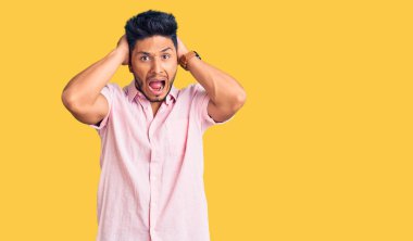 Yakışıklı Latin Amerikalı genç adam. Sıradan bir yaz gömleği giyiyor. Deli ve elleri başında korkmuş. 