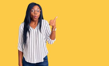 Gündelik giysiler ve gözlük takan Afro-Amerikalı genç bir kadın el parmağı yana dönük, ağzı açık şaşkın bir ifadeyle şaşırdı.. 