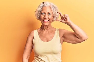 Yaşlı, gri saçlı, günlük kıyafetler giyen, gülümseyen, kendine güvenen, el hareketleriyle küçük beden işareti yapan, parmaklarını gösterip kameraya bakan bir kadın. ölçüm kavramı. 