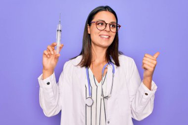 Steteskop takmış, elinde şırınga aşısı olan genç, güzel, esmer bir kadın parmak ucunda ağzı açık gülümsüyor.