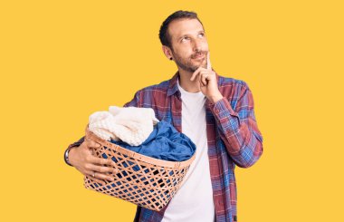 Çamaşır sepetini tutan yakışıklı genç adam ciddi bir yüz ifadesiyle eli çenesinde soruyu düşünüyor, kafa karıştırıcı bir fikir hakkında düşünceli. 