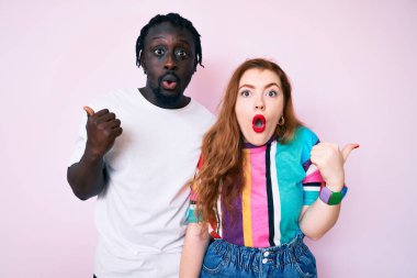 Irklar arası giysiler giyen çift, elleri yandan işaret ederek şaşırdı, ağzı açık hayret içinde kaldı.. 