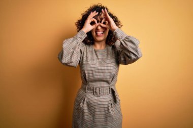 Güzel bir Arap iş kadını. Elbise ve gözlük takıyor. Sarı arka planda duruyor. Çılgın ifade.