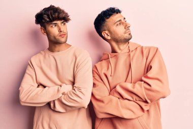 Gündelik giysiler giyen genç eşcinsel çift kollarını kavuşturmuş ve kendinden emin bir şekilde yan tarafa bakıyor. 