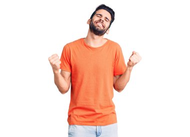 Sakallı, sıradan tişörtler giyen, çok mutlu ve heyecanlı genç bir adam kolları havada, gülümseyen ve başarı için çığlık atan, kazanan bir jest yapıyor. kutlama konsepti. 