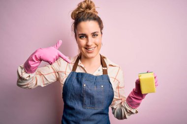 Güzel sarışın temizlikçi kadın ev işi yapıyor. Arpon ve eldiven takıyor. Suratı şaşkın bir şekilde kendini işaret ediyor.