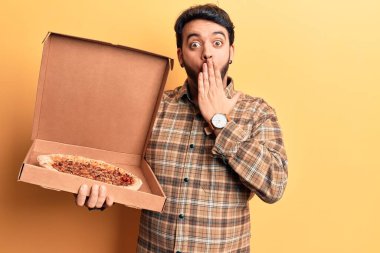 İspanyol asıllı genç adam elinde pizza kutusuyla ağzını eliyle kapatıyor, şok geçiriyor ve hata yapmaktan korkuyor. şaşırmış ifade 