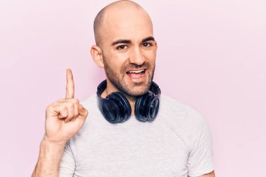 Genç yakışıklı kel adam müzik dinliyor kulaklıkla gülümsüyor bir fikir ya da soruyla gülümsüyor mutlu bir yüzle işaret ediyor, bir numara 