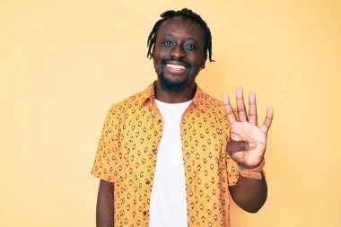 Saçları örgülü genç Afro-Amerikalı adam dört numarayı gösterip gösterirken kendinden emin ve mutlu gülümsüyor.. 