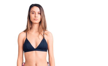 Yüzünde ciddi bir ifade olan bikini giyen genç ve güzel bir kız. Basit ve doğal bir şekilde kameraya bakıyorsun.. 