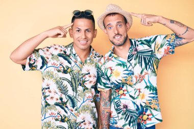 İki genç eşcinsel adam yaz şapkası ve Hawaii gömleği giyip gülümsüyor. İki eliyle başını işaret ediyor. Harika bir fikir ya da düşünce, iyi bir hafıza. 