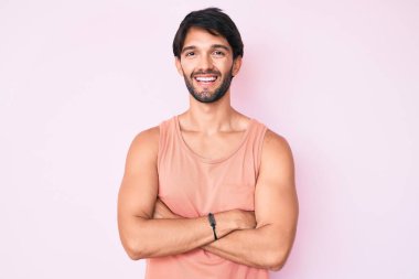 Yakışıklı, sıradan kıyafetler giyen mutlu yüzlü, kollarını kavuşturup kameraya bakan bir İspanyol. pozitif kişi. 