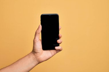 Kafkasyalı genç adam elinde akıllı telefonuyla izole edilmiş sarı arka planda ekranı gösteriyor.