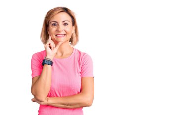 Spor giyinen genç sarışın kadın kameraya kendinden emin bakıyor kollarını kavuşturup gülümsüyor ve çenesini kaldırıyor. Olumlu düşünmek. 