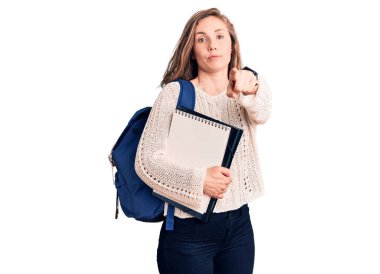 Genç, sarışın, öğrenci çantalı, elinde not defteri olan, kamerayı işaret eden bir kadın. Kendine güvenen, ciddi görünen bir jest. 