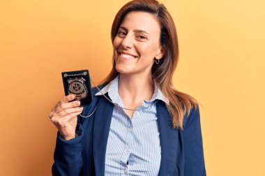 Dedektif rozeti tutan genç ve güzel bir kadın. Olumlu ve mutlu görünüyor. Kendine güvenen bir gülümsemeyle ayakta duruyor ve dişlerini gösteriyor. 