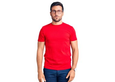 Yüzünde ciddi bir ifade olan günlük kıyafetler ve gözlük takan genç İspanyol bir adam. Basit ve doğal bir şekilde kameraya bakıyorsun.. 