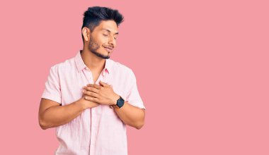 Yakışıklı Latin Amerikalı sıradan bir yaz tişörtü giymiş elleri göğsünde, gözleri kapalı ve yüzünde minnet ifadesi olan genç bir adam. sağlık kavramı. 