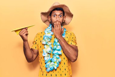 Yaz şapkası takan genç bir latin ve elinde kağıt uçakla ağzı kaplayan Hawaii zambağı tutan bir adam. Şok olmuş ve hata yapmaktan korkuyor. şaşırmış ifade 